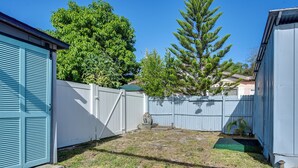 Un cortile recintato con un piccolo giardino, un albero e un edificio con una porta blu.