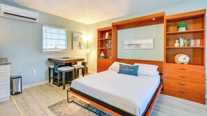 Un dormitorio con cama, escritorio, silla, un pequeño cubo de basura y estantería.