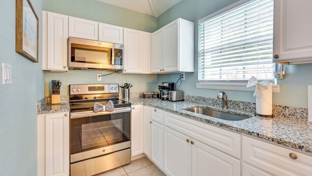 A kitchen with white cabinets, a stainless steel oven, a microwave, a coffee maker, and a window with blinds. - 7 Mi to Historic Dtwn! New Port Richey Cottage (New Port Richey)