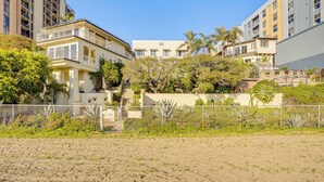 A multi-story residential building with balconies, surrounded by lush greenery and a sandy foreground. - Beachfront Living in Long Beach: 2,500 Sq Ft Condo (Long Beach)