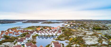 A coastal village with white houses and red roofs, surrounded by rocky terrain and a calm body of water.