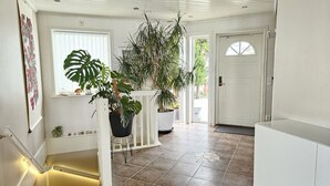 Een ruime hal met een witte trap, potplanten en een deur naar een andere kamer.
