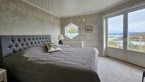 Een slaapkamer met een groot bed, een raam met uitzicht en een kleine tafel met een lamp.