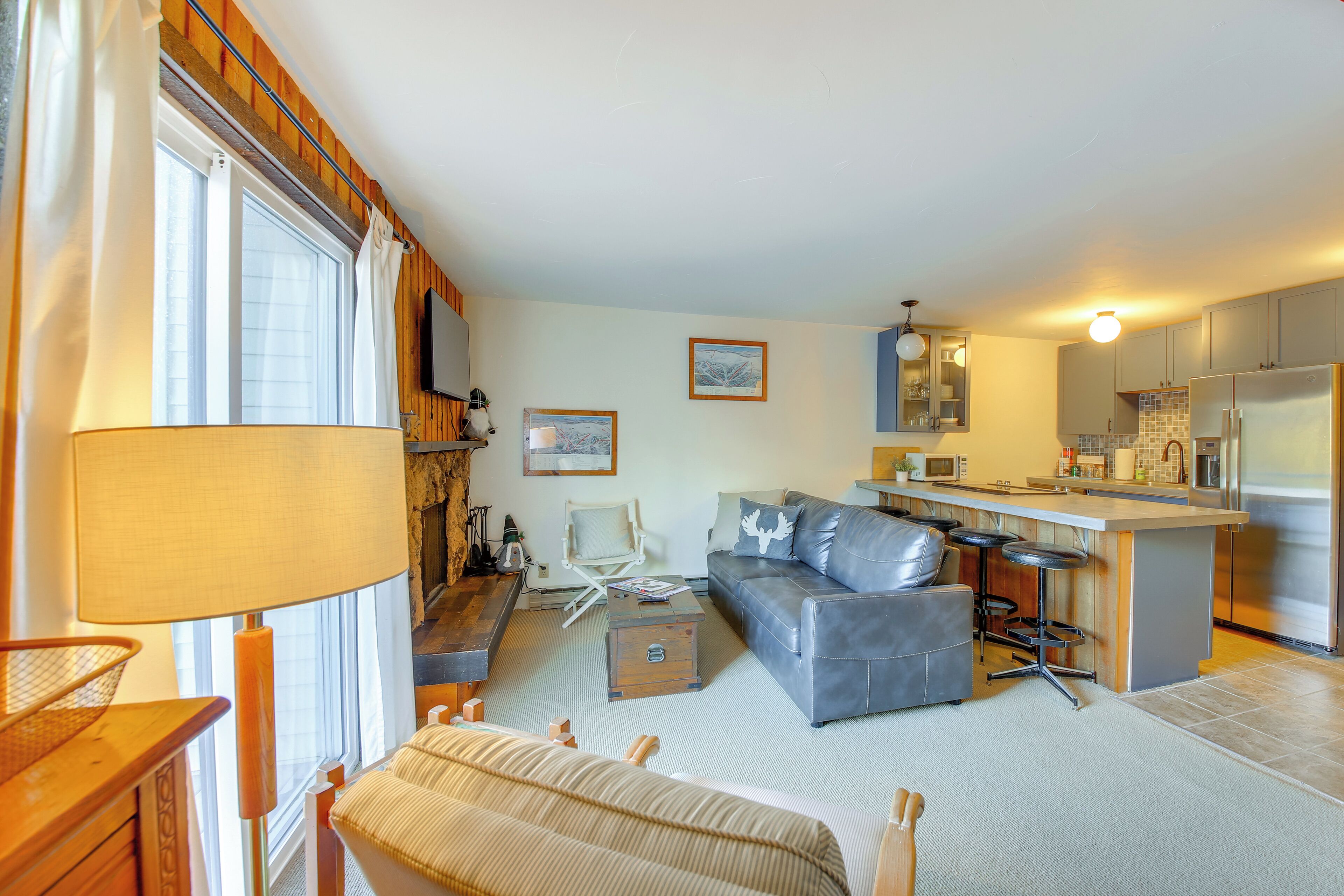 A living room with a sofa, a coffee table, and a TV. There is a kitchen area with a refrigerator and a microwave.