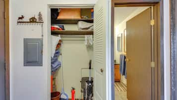 A narrow hallway with a closet containing folded clothes, a vacuum cleaner, and a broom.
