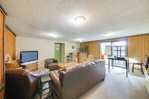 Un salon avec un canapé en cuir marron, un téléviseur, un meuble en bois et un coin repas comprenant une table et des chaises.