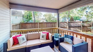 A covered outdoor seating area with wicker furniture and cushions, overlooking a backyard with a wooden deck and trees. - 3BR Dog-friendly Retreat w/ Fireplace & Patio (Annapolis)