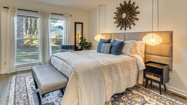 A bedroom with a large bed, a bench, a nightstand, and a wall-mounted lamp. - Quiet & Modern Family Home in Spring Lake (Spring Lake)