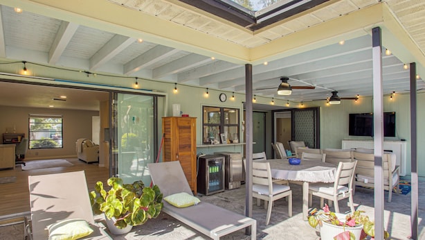 A spacious indoor area with a glass wall, a dining table with chairs, a lounge chair, and a ceiling fan. - Port Charlotte Home w/ Heated Pool & Yard! (Port Charlotte)