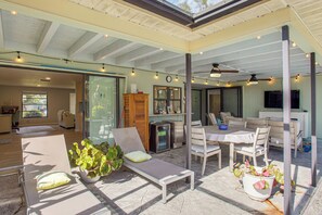 A spacious indoor area with a glass wall, a dining table with chairs, a lounge chair, and a ceiling fan. - Port Charlotte Home w/ Heated Pool & Yard! (Port Charlotte)