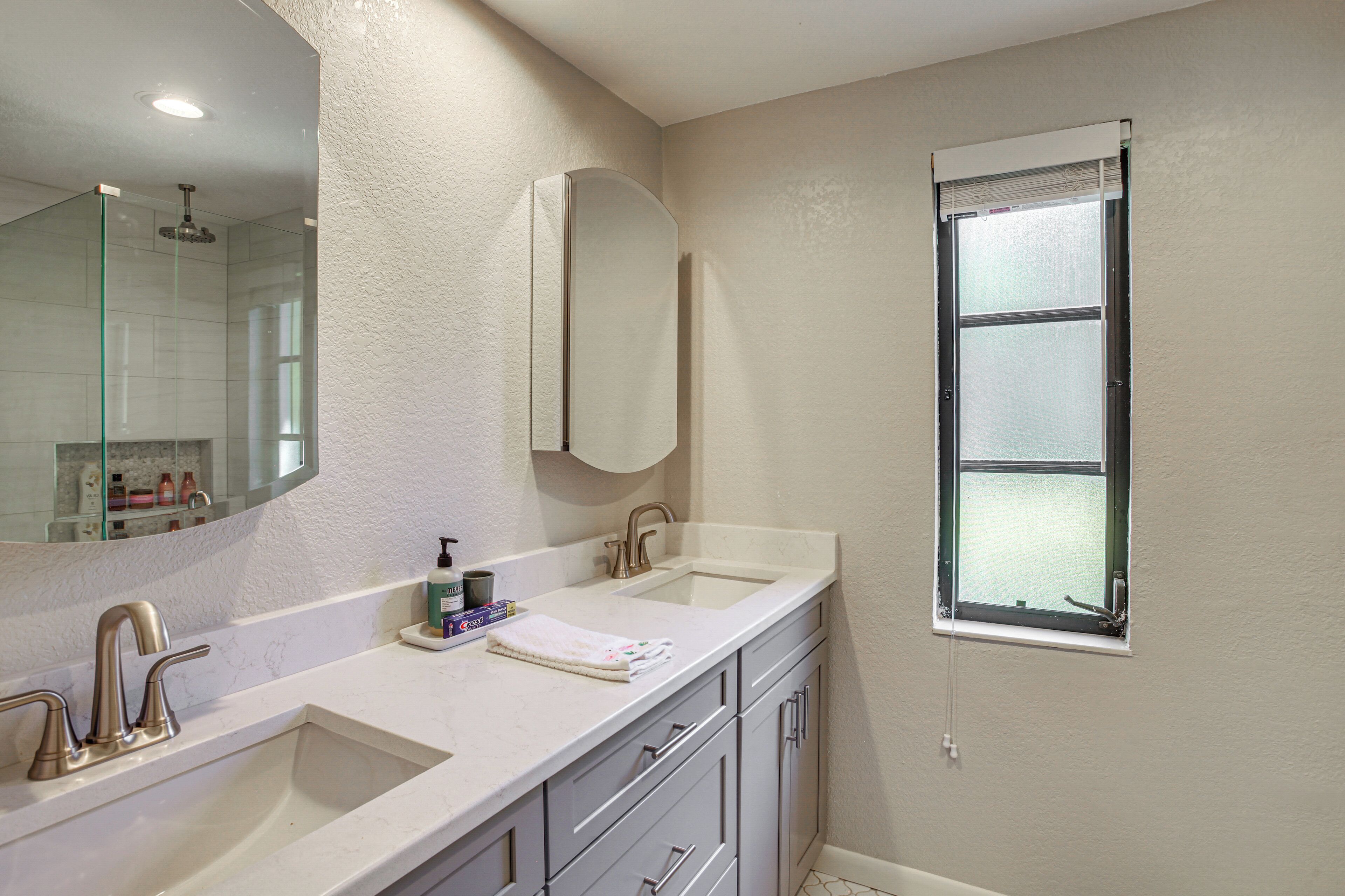 A bathroom with two sinks, a large mirror, and a window.