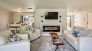 A living room with a fireplace, white sofas, a coffee table, and a TV mounted above the fireplace. - Port Charlotte Home w/ Heated Pool & Yard! (Port Charlotte)