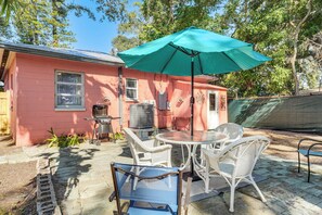 A patio with a table and chairs, a grill, and a pink house in the background. - 5 Mi to St Pete Beach! Snowbird Home w/ Large Yard (St. Petersburg)