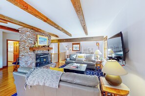 Uma sala de estar ampla com lareira, um sofá, uma mesa de centro e uma TV fixada na parede.