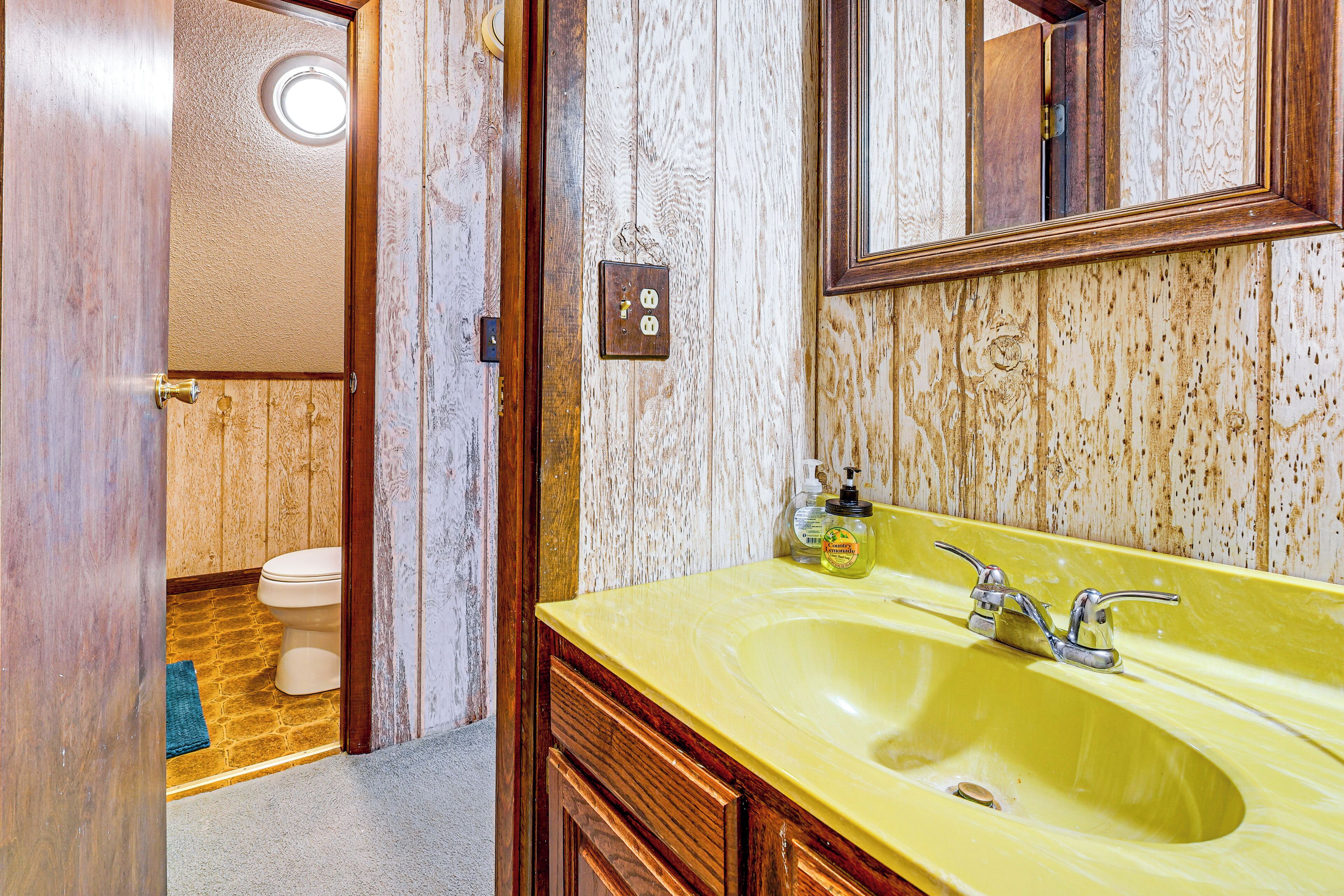 A bathroom with a yellow sink, wooden cabinets, and a mirror.