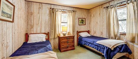 Una habitación con dos camas, paredes de madera, un aparador y una ventana con cortinas.