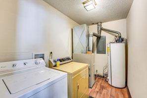 Une buanderie équipée d’un lave-linge à chargement frontal, d’un sèche-linge, d’un chauffe-eau et d’un meuble de rangement pour les produits d’entretien.