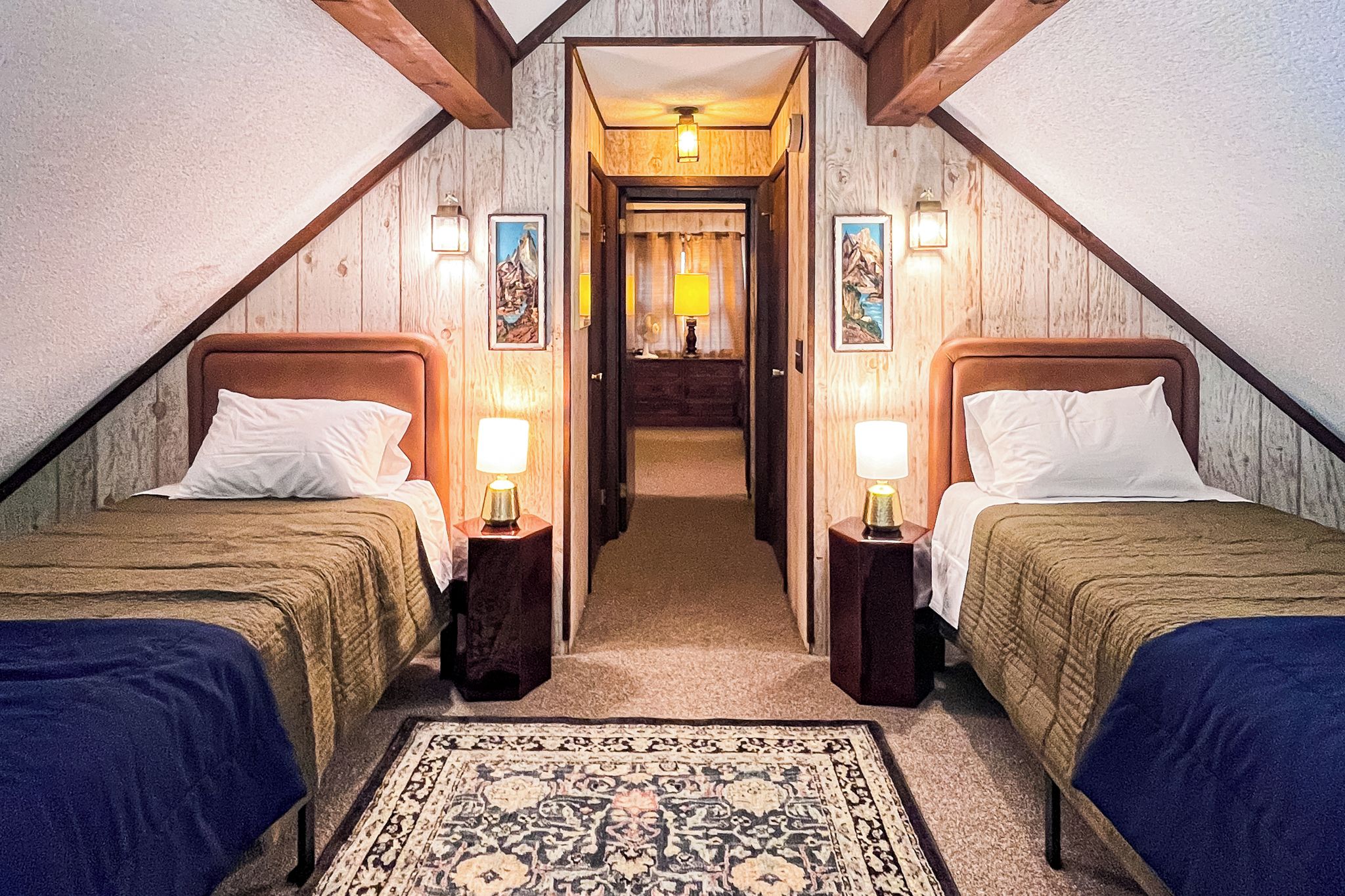 A room with two beds, a carpet, and a hallway leading to a bathroom.