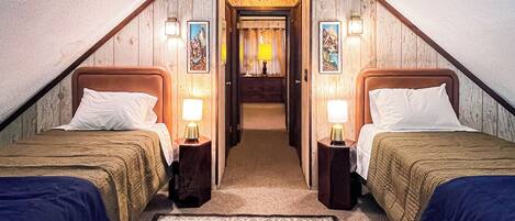 A room with two beds, a carpet, and a hallway leading to a bathroom.