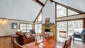 Une pièce spacieuse avec une grande table à manger en bois, des sièges confortables, une cheminée et de grandes fenêtres donnant sur l’extérieur.