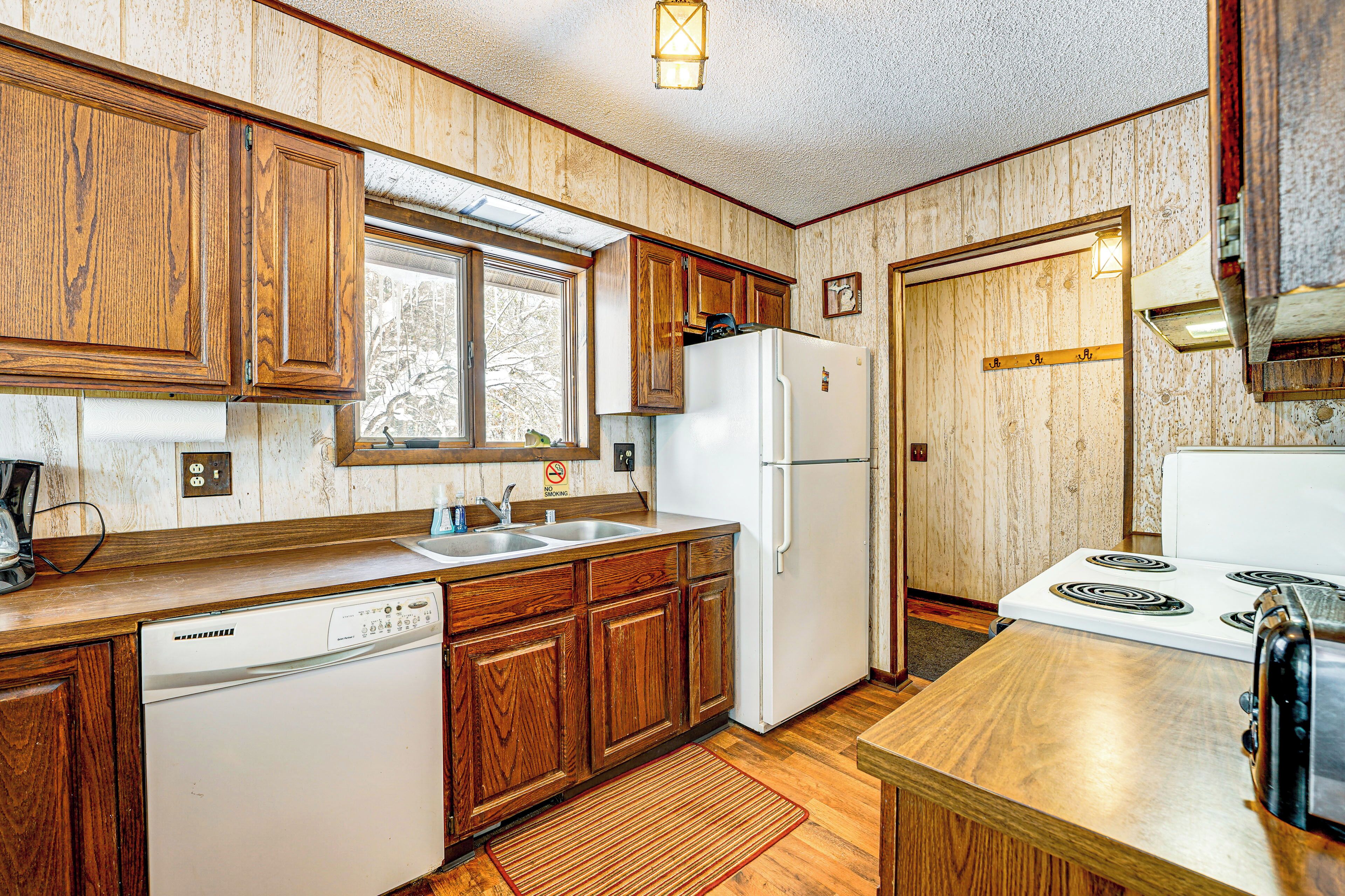 A kitchen with wooden cabinets, a dishwasher, a refrigerator, a stove, and a window.