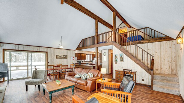 Un vaste salon doté d’un haut plafond, de poutres en bois, d’un escalier et offrant une vue sur l’extérieur.
