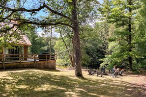 A wooden cabin with a deck, surrounded by trees and a grassy area with benches. - Pere Marquette Riverfront Cabin w/ Fishing Access (Branch)