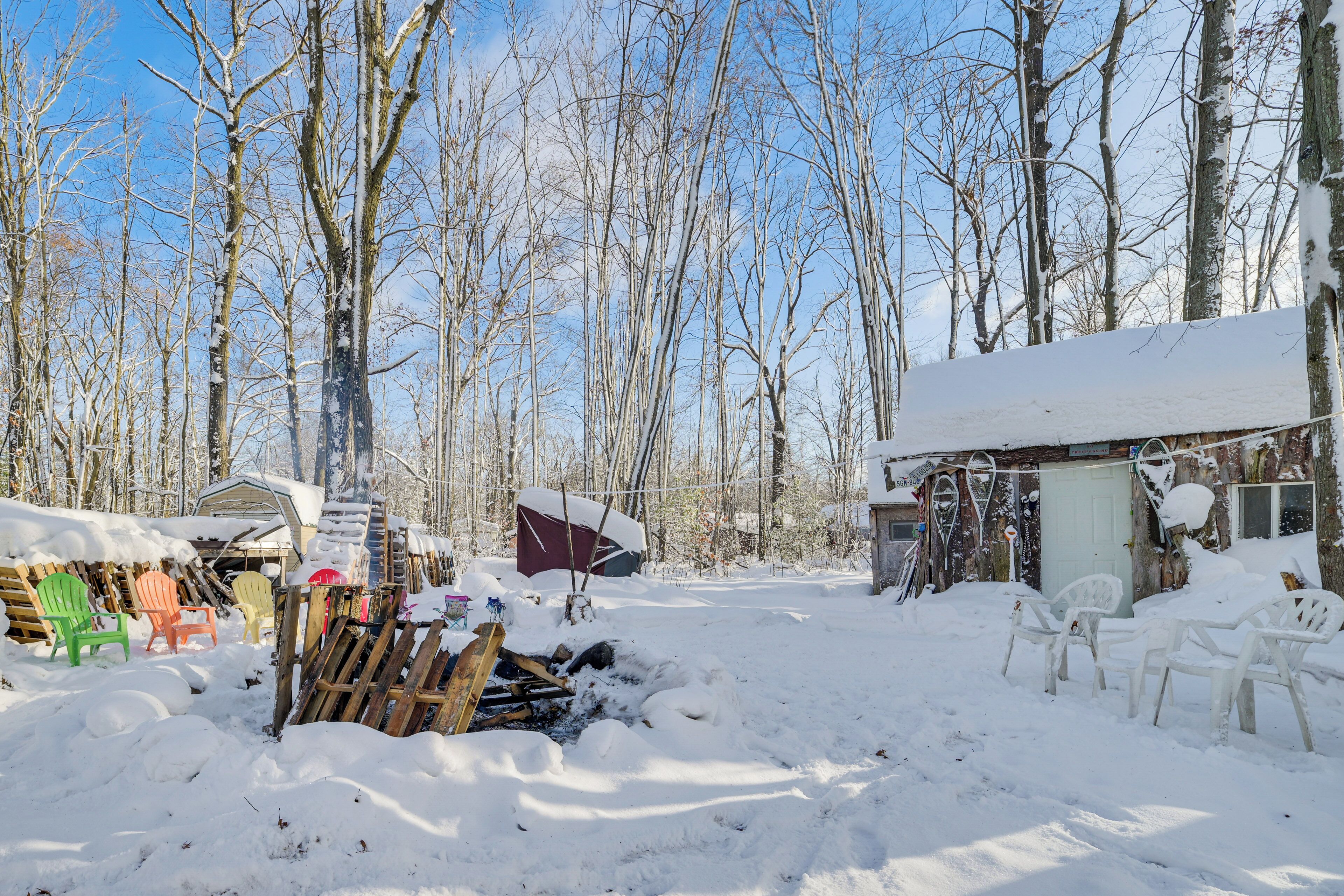 A snowy outdoor area with a wooden deck, several Adirondack chairs, and a small shed.