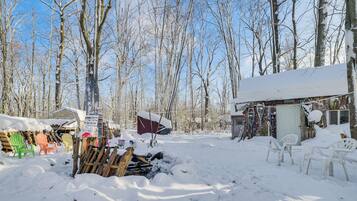 A snowy outdoor area with a wooden deck, several Adirondack chairs, and a small shed.
