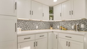 Una cocina moderna con gabinetes blancos, salpicadero blanco y negro, y varios utensilios de cocina sobre la encimera.