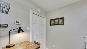 Une pièce avec un bureau en bois, une lampe noire, une porte blanche et un thermostat fixé au mur.