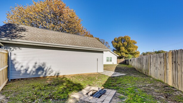Un jardin à l’arrière d’une maison, avec un garage, une clôture en bois et un arbre aux feuilles d’automne.