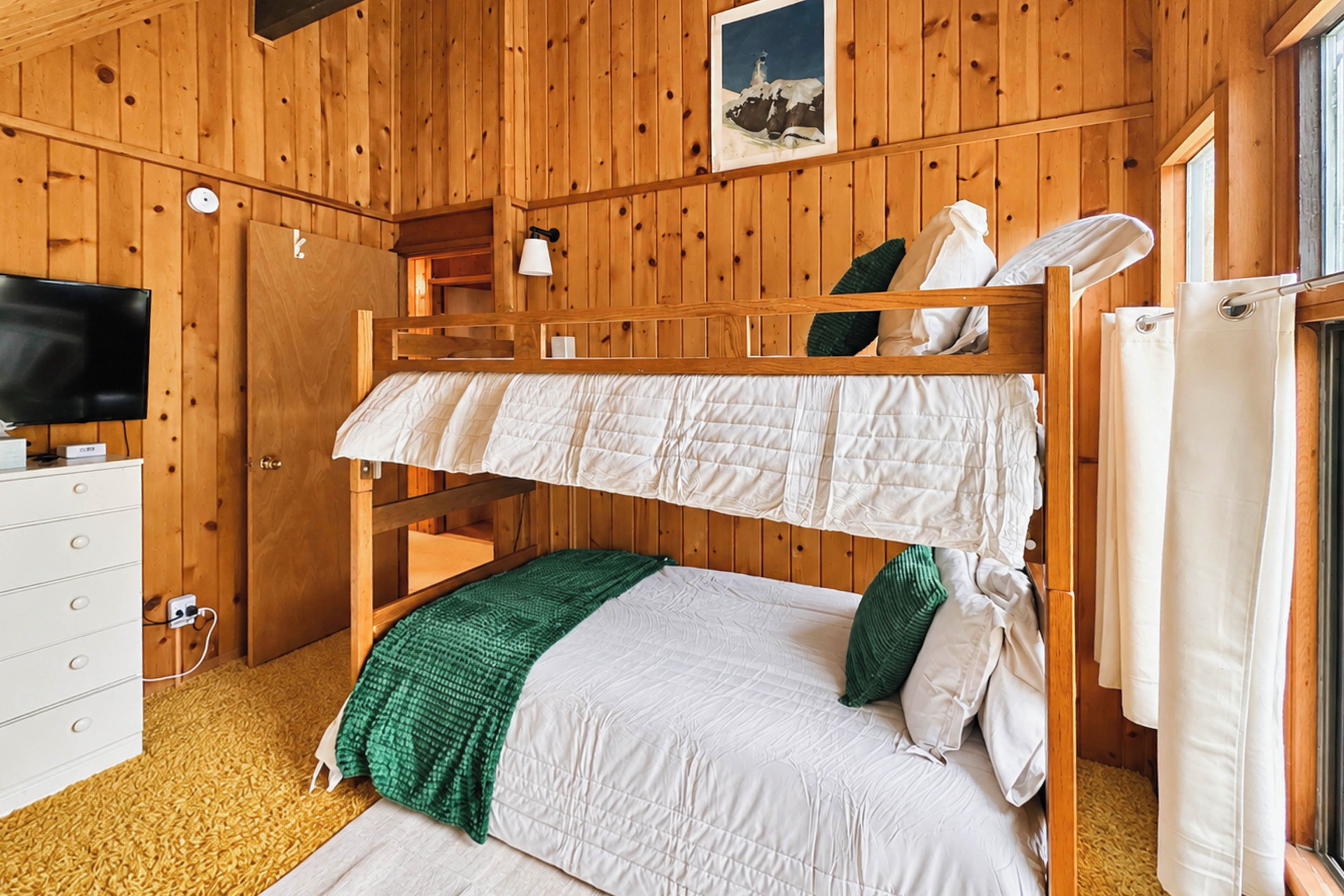 A bunk bed room with a television, a dresser, and a window with curtains.