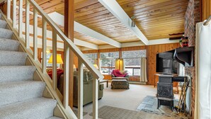 A cozy cabin interior with a wooden staircase, a fireplace, and a large window offering a view of the snowy outdoors. - Outdoor Adventure Hub! Family Home in West Dover (West Dover)