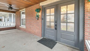 A brick exterior with a gray double door, a white porch railing, and a ceiling fan. - Walk to Marshall University: Home w/ Private Yard! (Huntington)