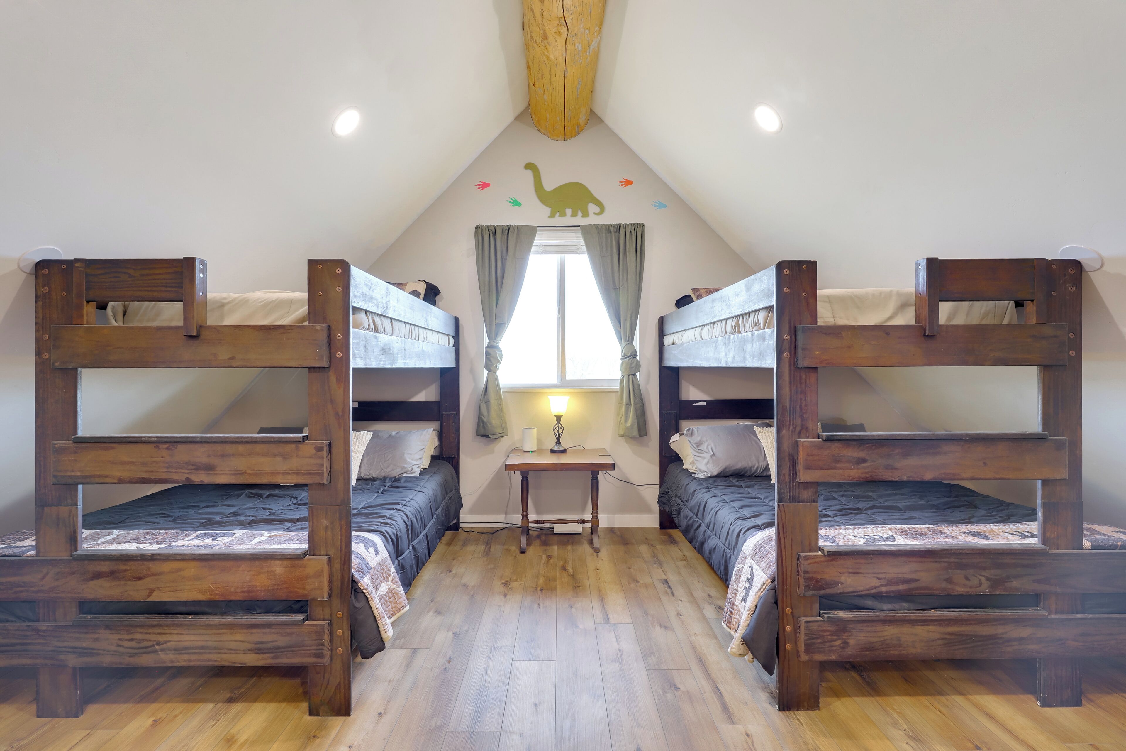 A room with two bunk beds, a small table with a lamp, and a window with curtains.