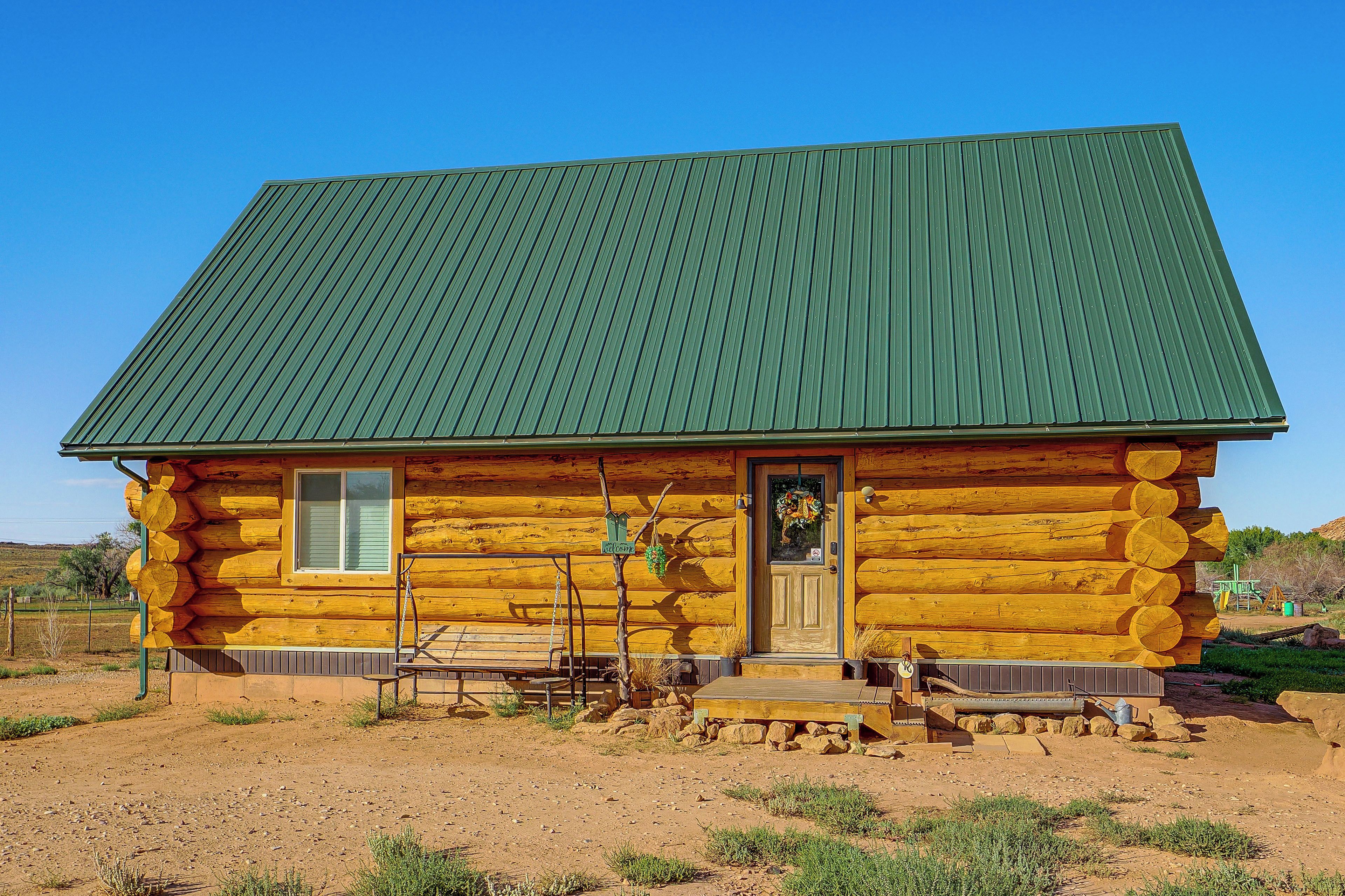 A log cabin with a green metal roof, a wooden front door, and a bench outside.