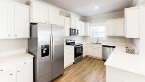 A modern kitchen with white cabinetry, stainless steel appliances, and a wooden floor. - Steps to Beach! St Teresa Retreat w/ Pool Access (Carrabelle)