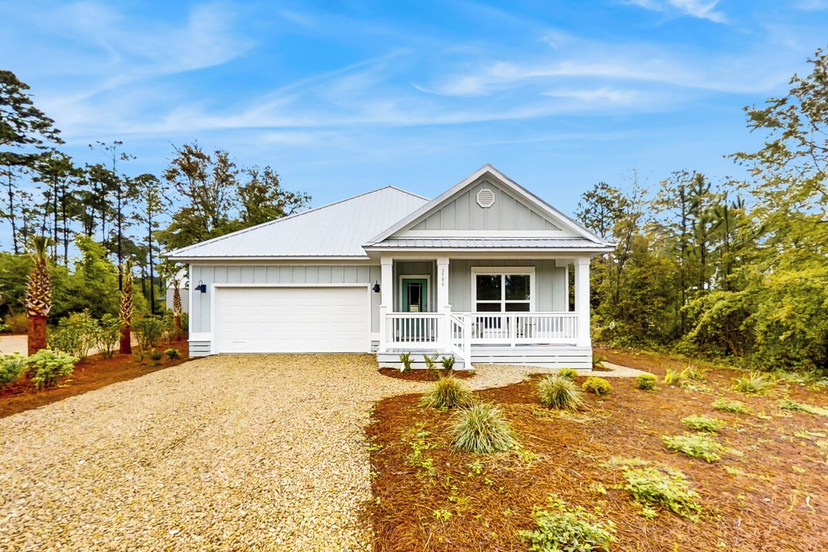 A single-story house with a white exterior, a front porch, and a gravel driveway.