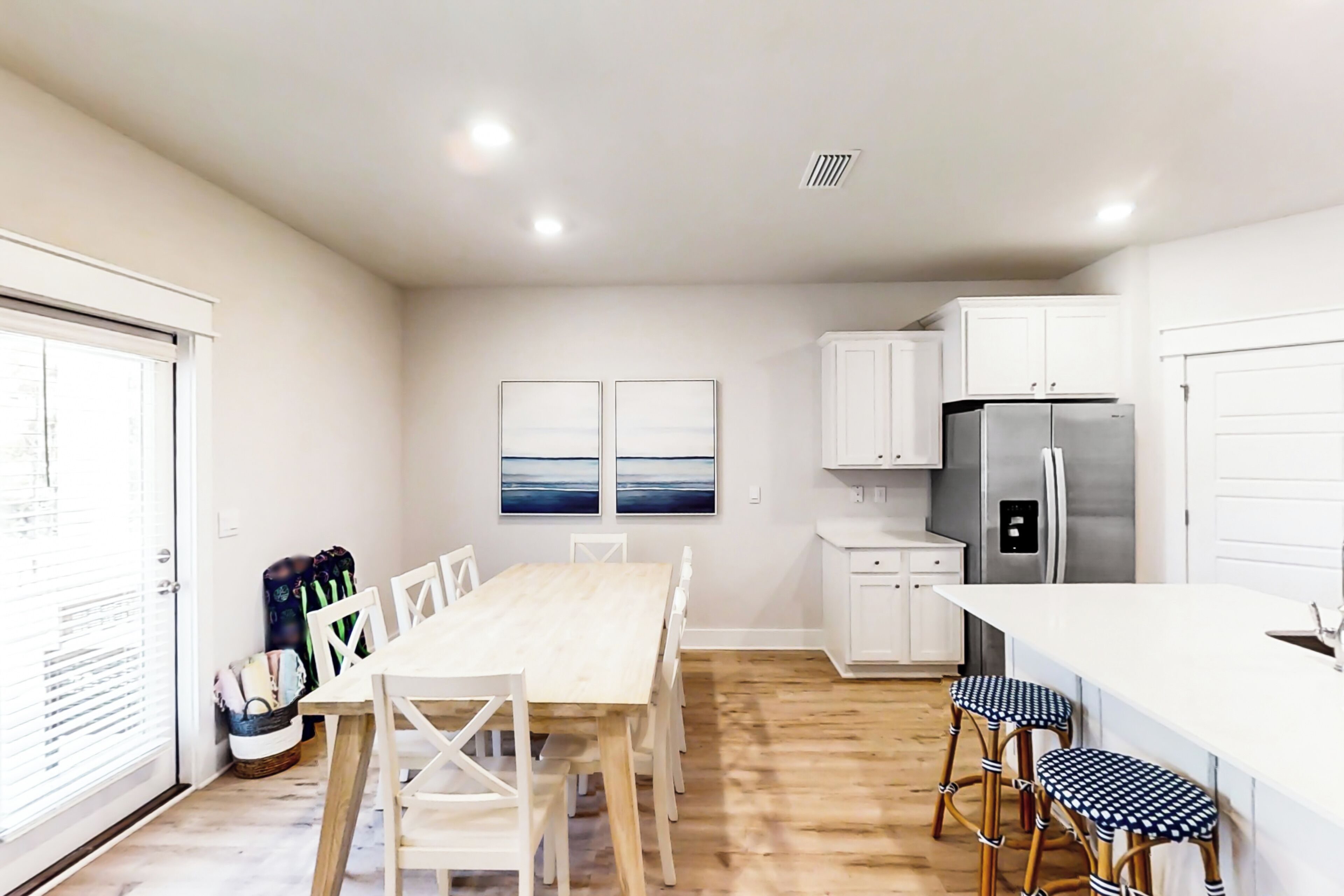 A modern kitchen with white cabinets, a stainless steel refrigerator, and a wooden dining table with white chairs.
