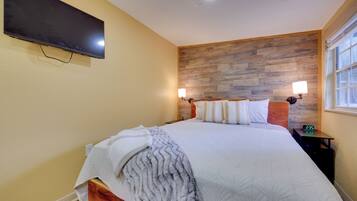 A bedroom with a large bed, a mounted TV, a wooden headboard, bedside lamps, and a window with a view.