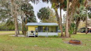 A small yellow building with a porch, surrounded by trees and grass. - Hawthorne Angler's Cabin w/ Lake + Dock Access! (Hawthorne)