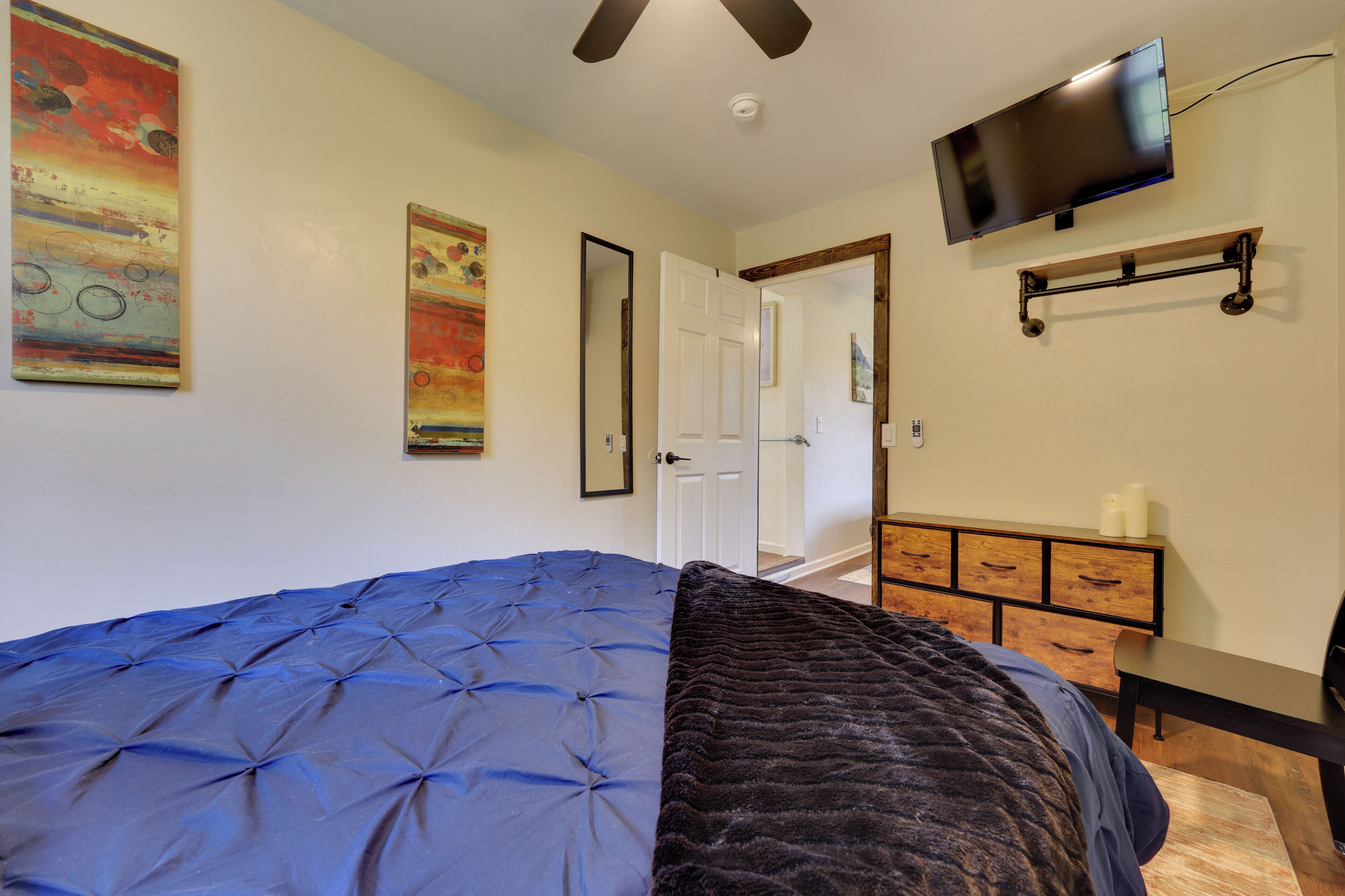 Une chambre avec un grand lit, un téléviseur fixé au mur et une commode en bois.
