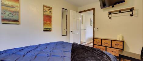 Une chambre avec un grand lit, un téléviseur fixé au mur et une commode en bois.