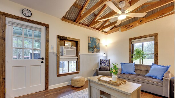 A cozy living room with a wooden ceiling, a white door, a sofa with blue cushions, and a coffee table with a vase and a tray. - Hawthorne Angler's Cabin w/ Lake + Dock Access! (Hawthorne)