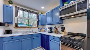 A kitchen with blue cabinets, a stove, a microwave, and a window with blinds. - Hawthorne Angler's Cabin w/ Lake + Dock Access! (Hawthorne)
