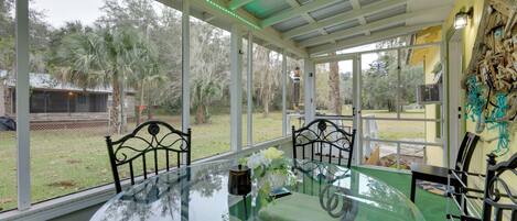 A glass-enclosed dining area with a round table, chairs, and a view of the outdoors.