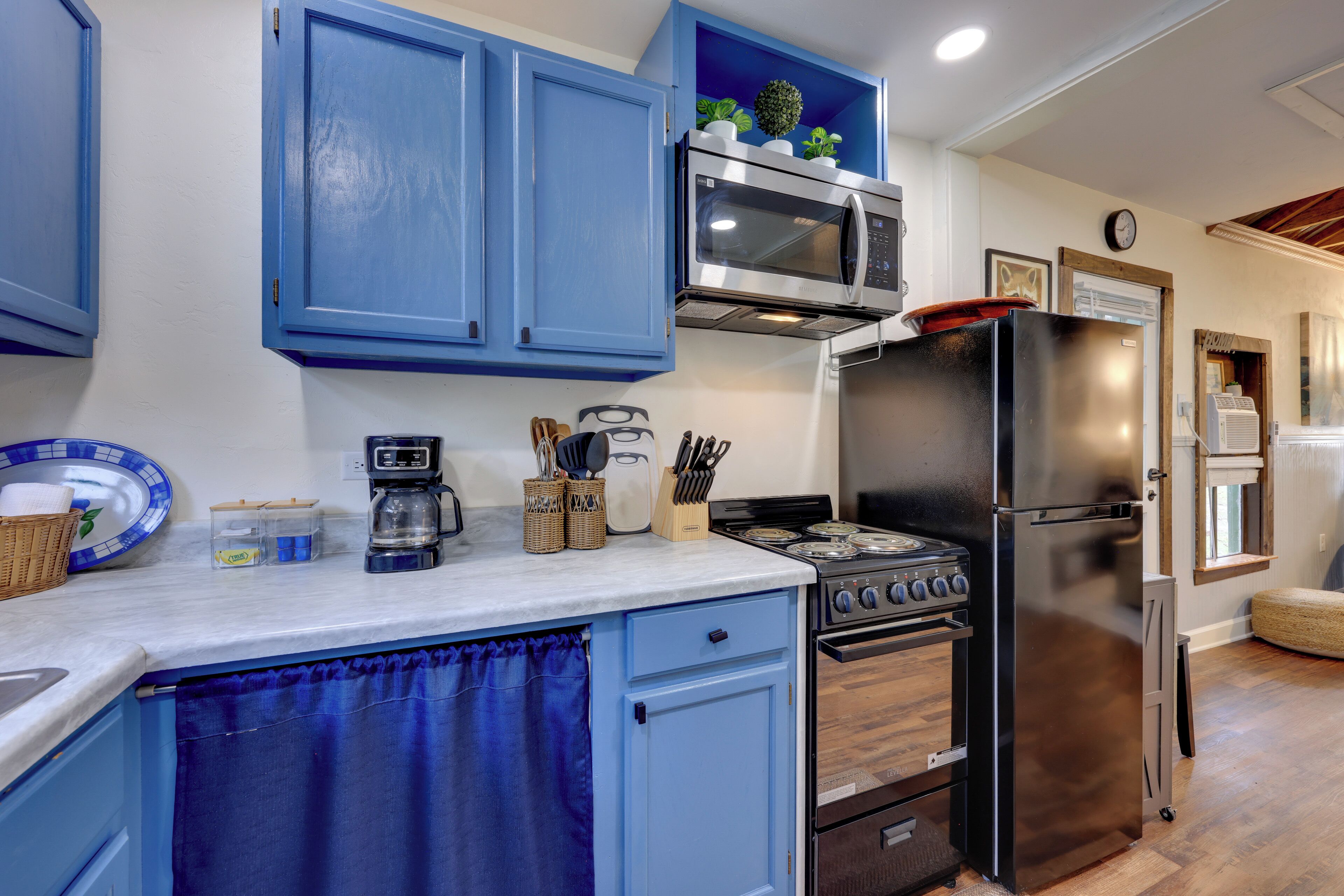 A kitchen with blue cabinets, a stainless steel refrigerator, a microwave, and a stove.