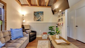 A living room with a sofa, a chair, a TV mounted on the wall, a plant, and a wooden table with magazines. - Hawthorne Angler's Cabin w/ Lake + Dock Access! (Hawthorne)