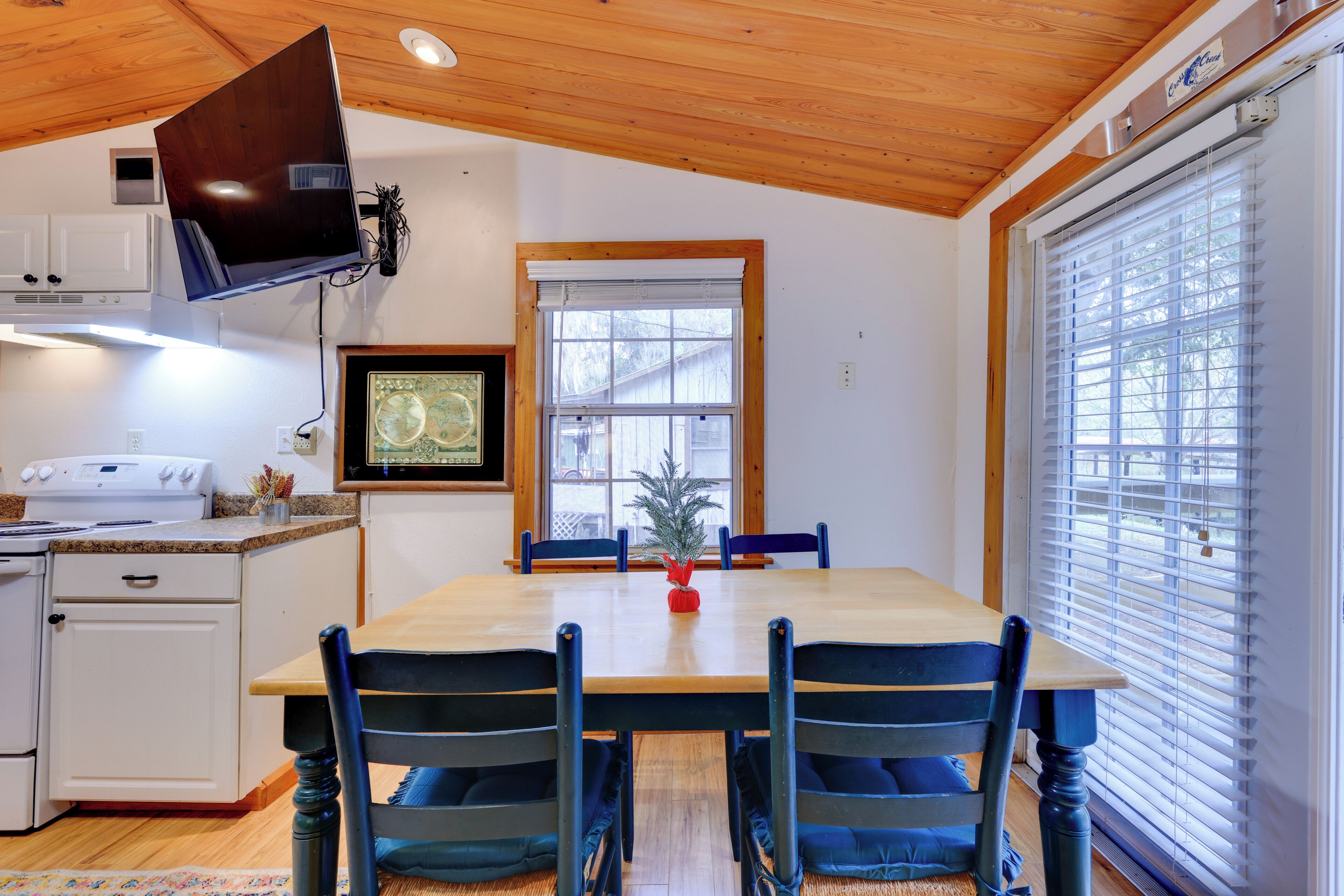 A dining area with a wooden table and chairs, a kitchen with a stove and cabinets, and a window with blinds.